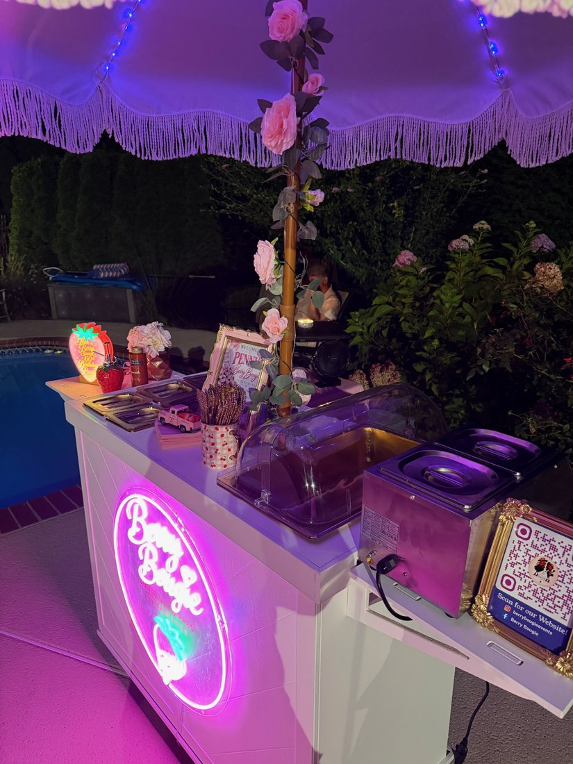 Berry Bougie cart glowing with neon sign beside a pool at night
